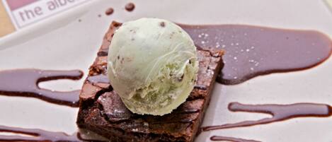 Un dessert composé d’une part de brownie surmontée d’une boule de glace, le tout nappé de sauce au chocolat, présenté sur une assiette avec une carte de l’hôtel.