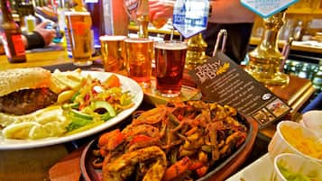 A bar setting with a variety of dishes, including a plate of grilled meat, a salad, and a bowl of soup. There are multiple beer taps and glasses visible.