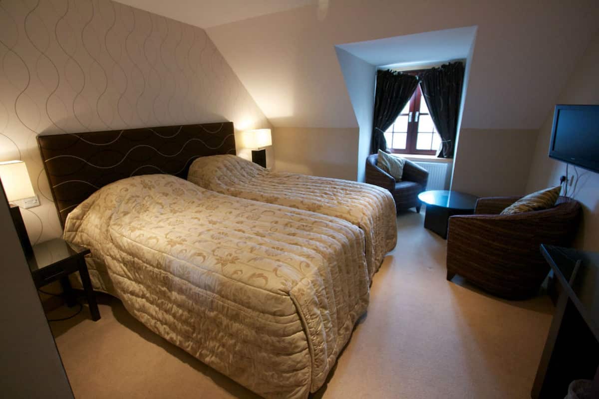 A hotel room with two beds, a desk, a chair, a TV, and a window with curtains.