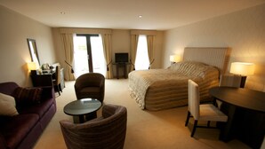 A hotel room with a large bed, a sofa, a chair, a small table, and a desk with a lamp.