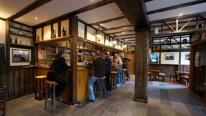 A bar area with wooden beams, stone flooring, and stools.