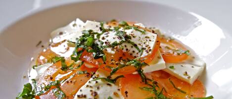 Een witte schaal met een salade van tomaten, mozzarella en kruiden.