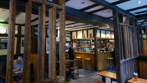 A rustic interior with exposed wooden beams, a bar area, and seating for patrons.