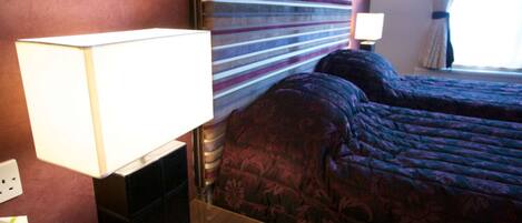 A hotel room with a large bed, a bedside table with a lamp, and a nightstand.