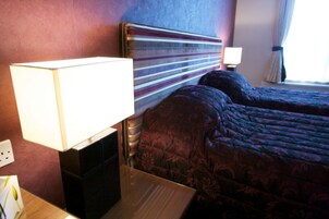 A hotel room with a large bed, a bedside table with a lamp, and a nightstand.