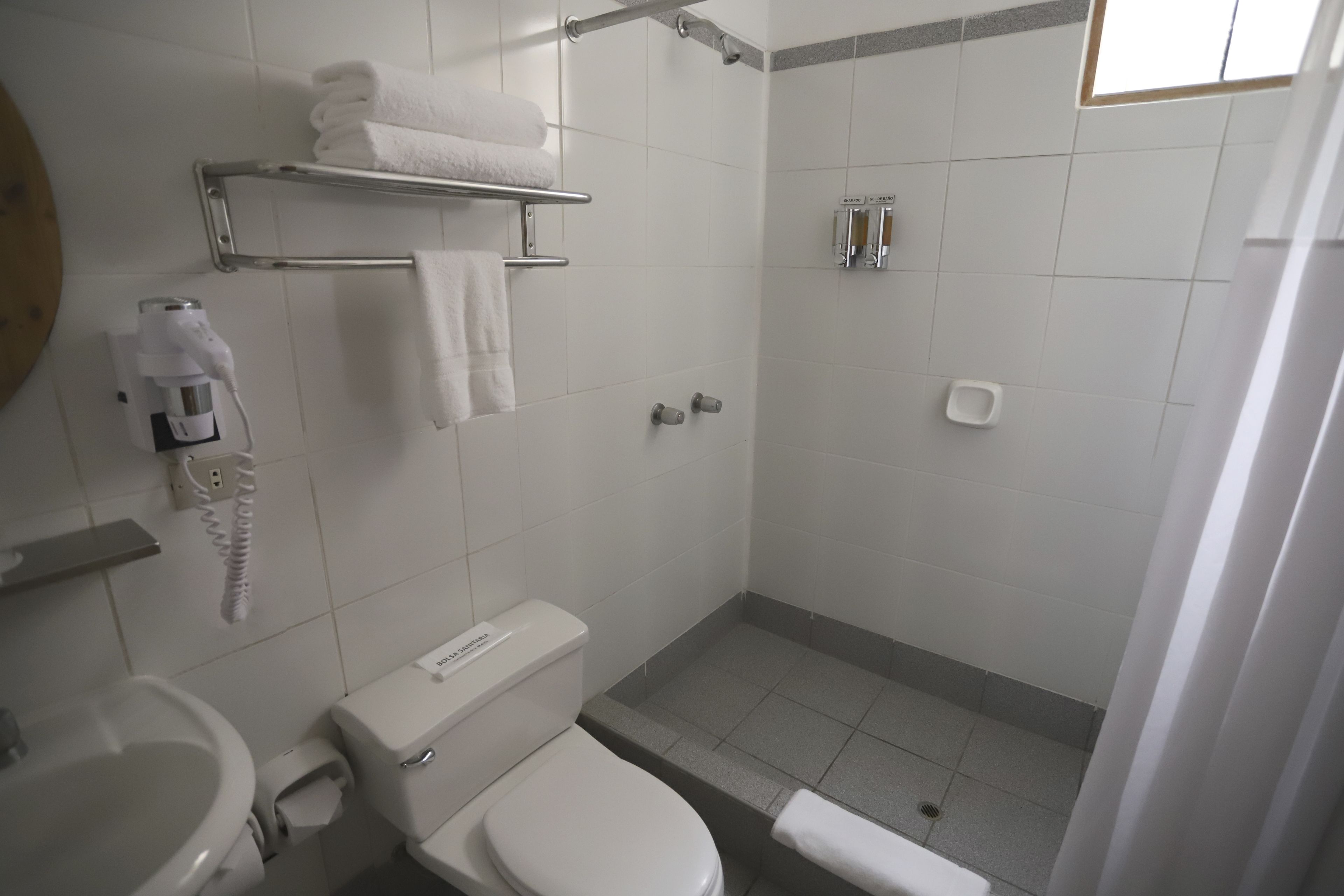 A bathroom with a toilet, sink, towel rack, and shower area.
