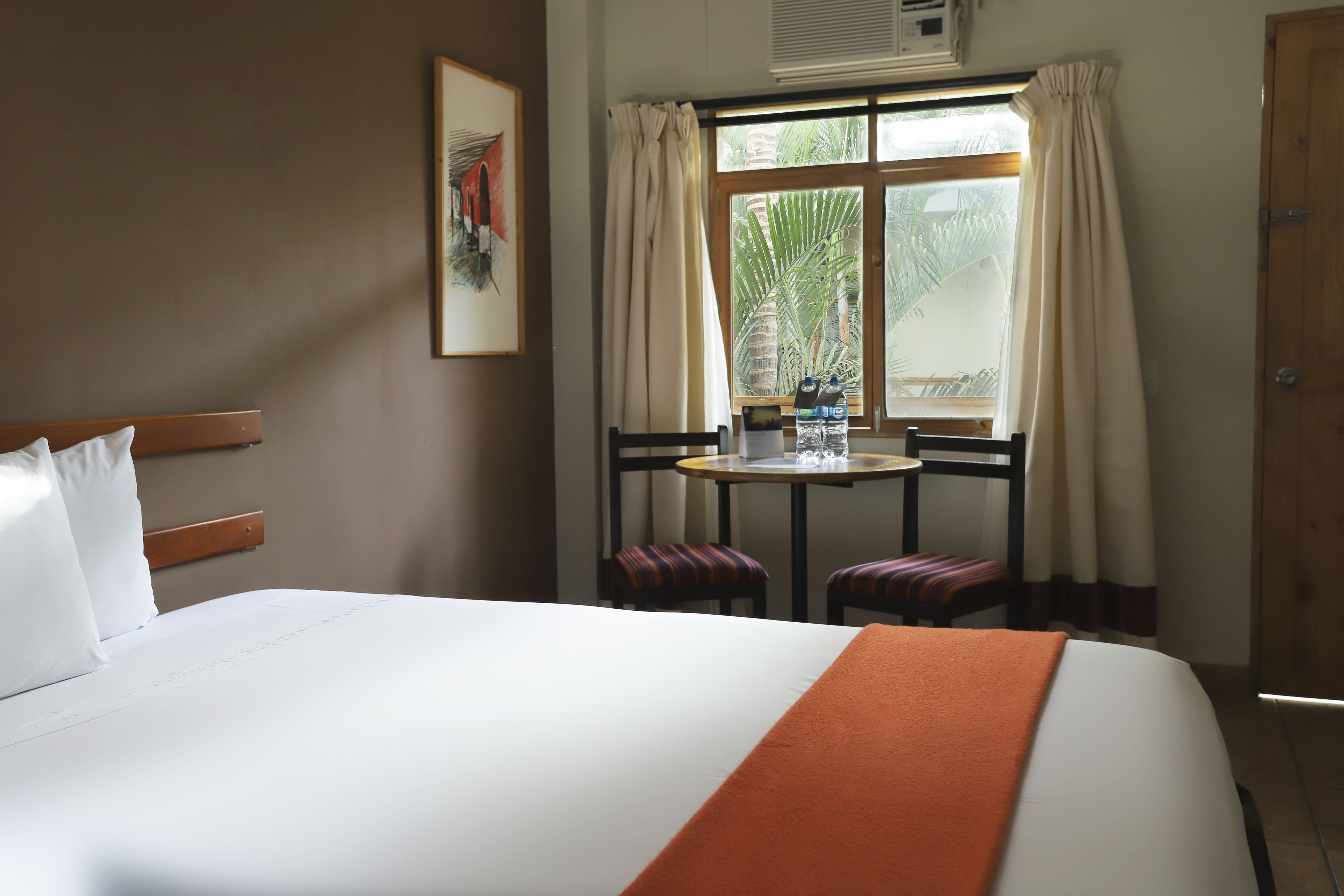Una habitación de hotel con cama, una mesa con sillas, un ventanal con cortinas y una puerta.
