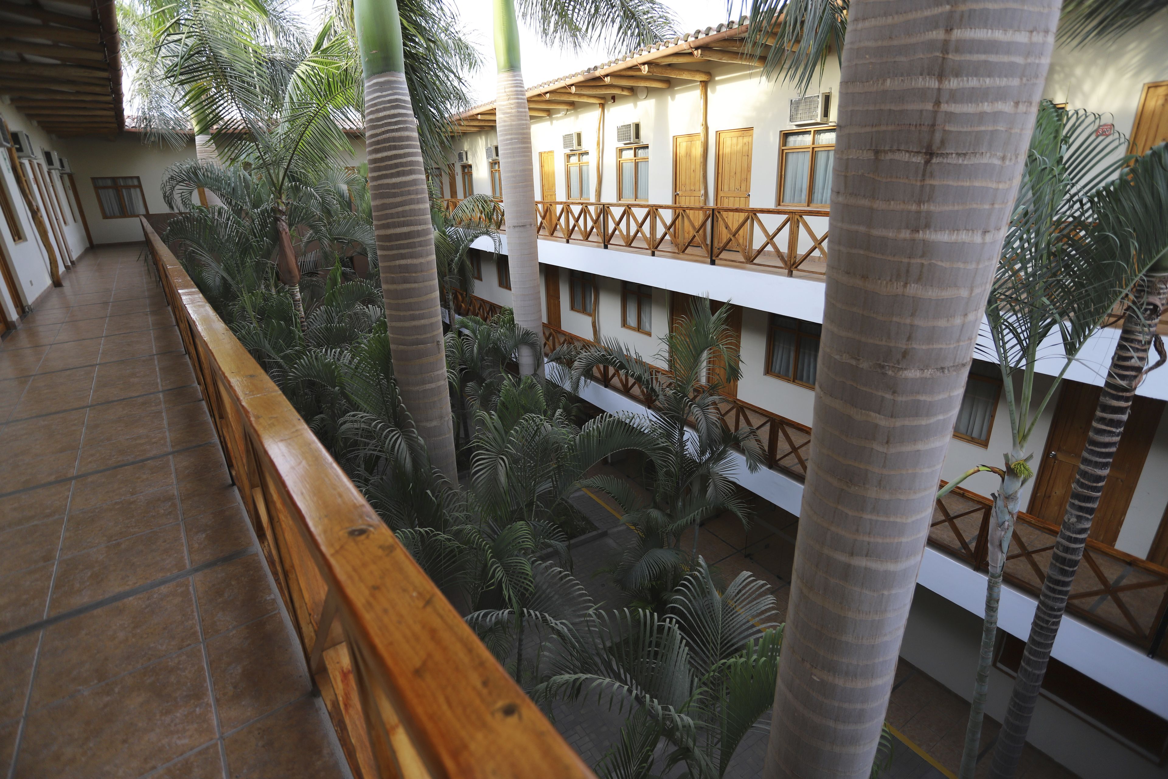 Un edificio de varios niveles con balcones de madera y un atrium central lleno de palmeras.