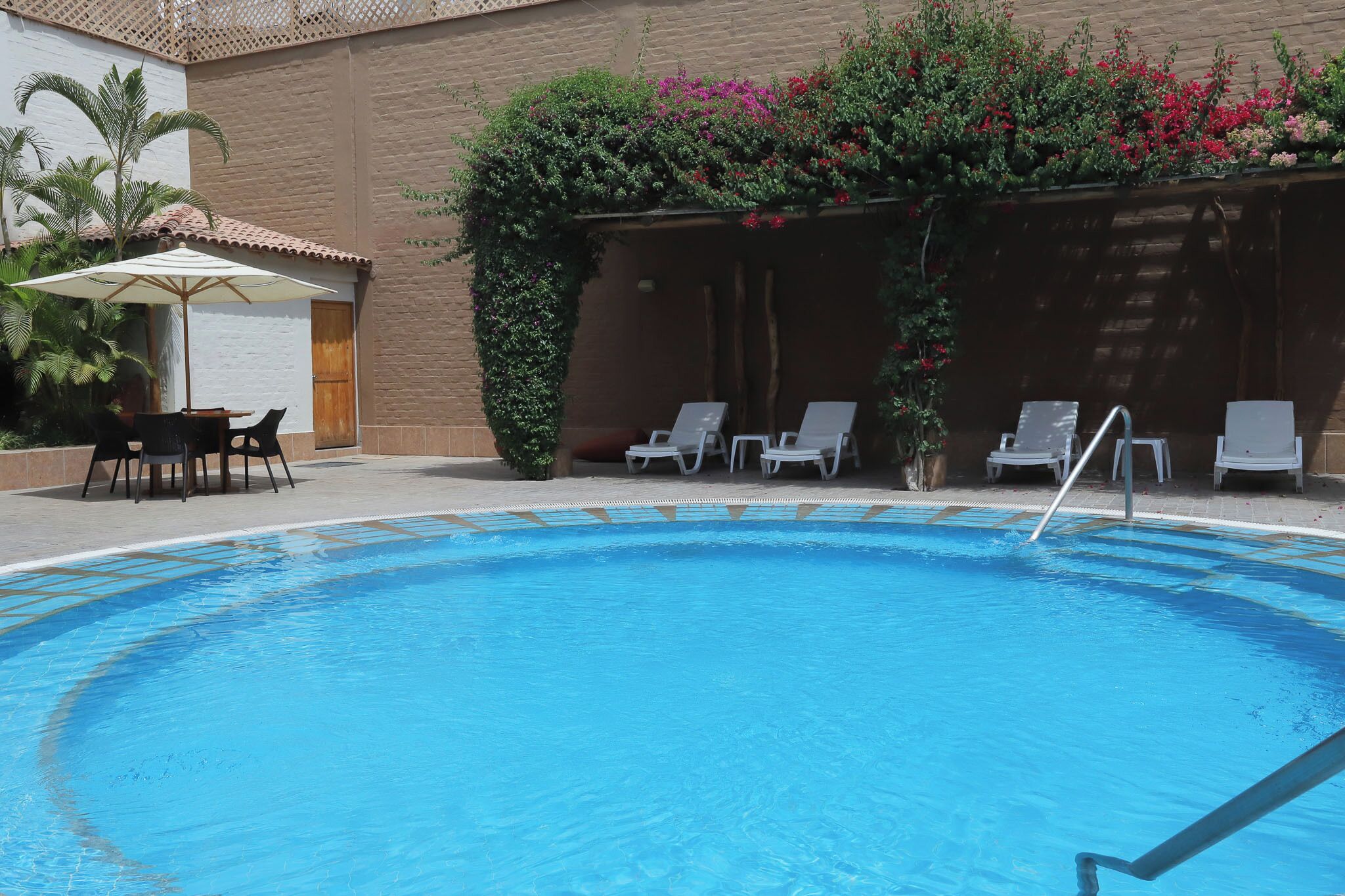 Una piscina amb gandules i una taula, envoltada de plantes i flors.