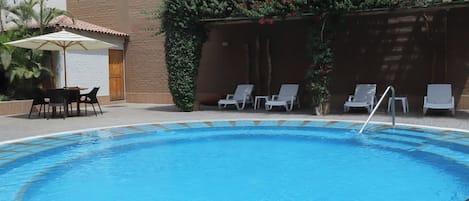 A swimming pool with lounge chairs and a table, surrounded by plants and flowers.