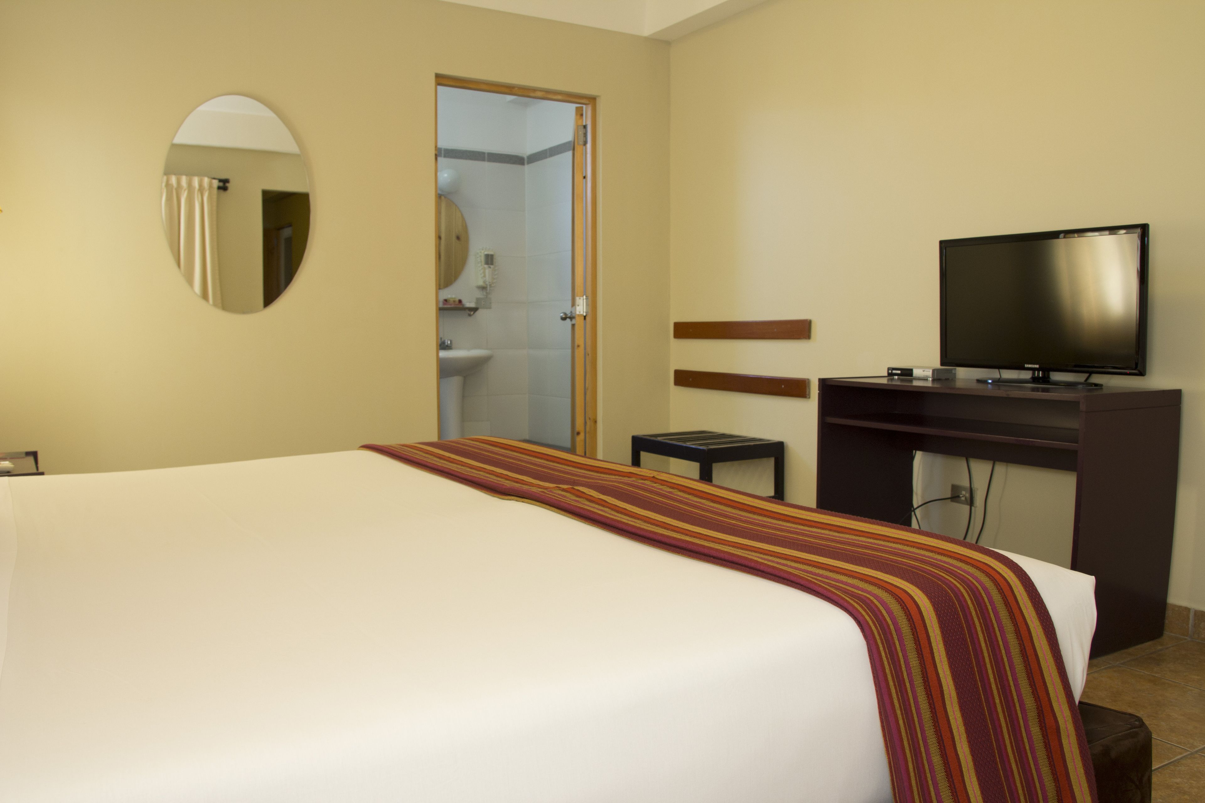 Habitación de hotel con cama, televisión, escritorio y baño visible a través de una puerta abierta.