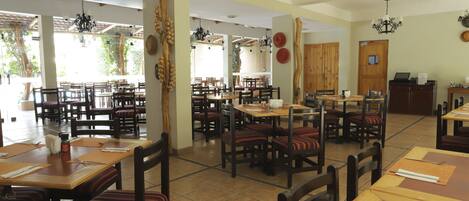 A spacious restaurant with multiple dining tables and chairs, large windows, and a ceiling fan.