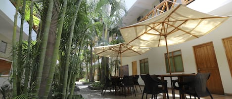 Un patio interior con plantas de bambú, mesas y sillas al aire libre bajo grandes sombrillas.