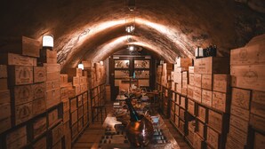 An underground storage area with wooden crates stacked on shelves, a central aisle, and a vintage-style light fixture. - Hôtel & SPA Les Violettes (Soultz-Haut-Rhin)