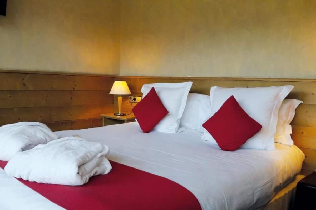 A neatly made bed with white and red bedding, two pillows, and two towels. There are two bedside lamps on wooden nightstands.