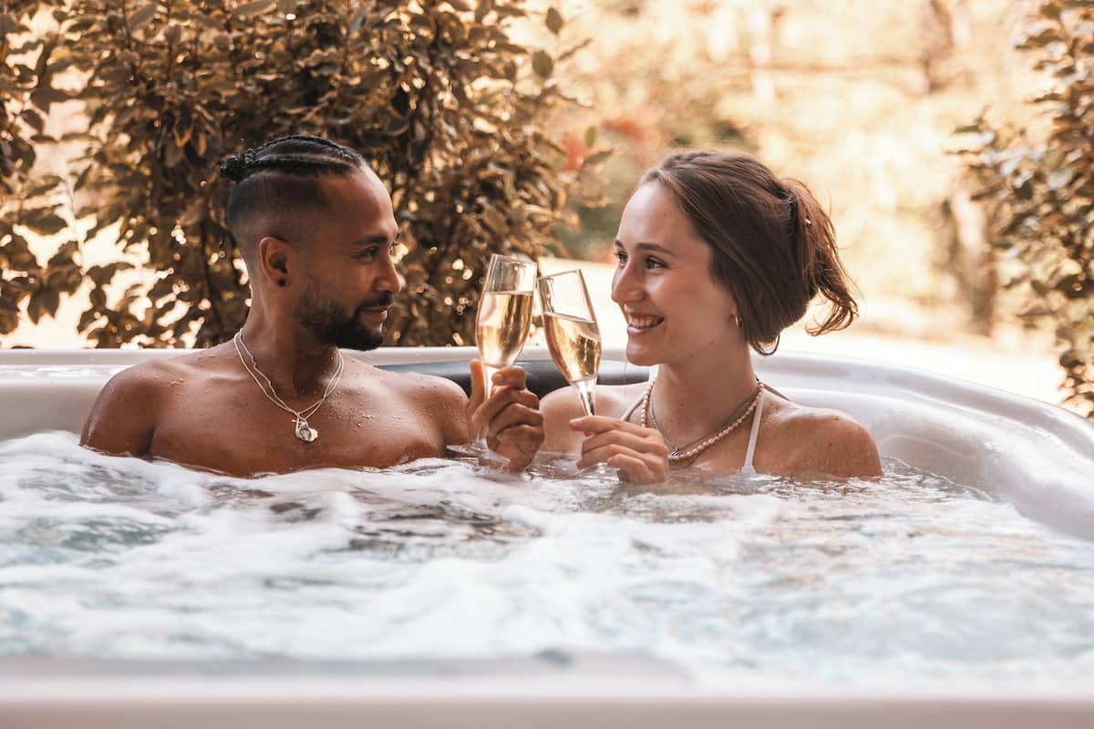 Two people in a hot tub with bubbles, surrounded by greenery.