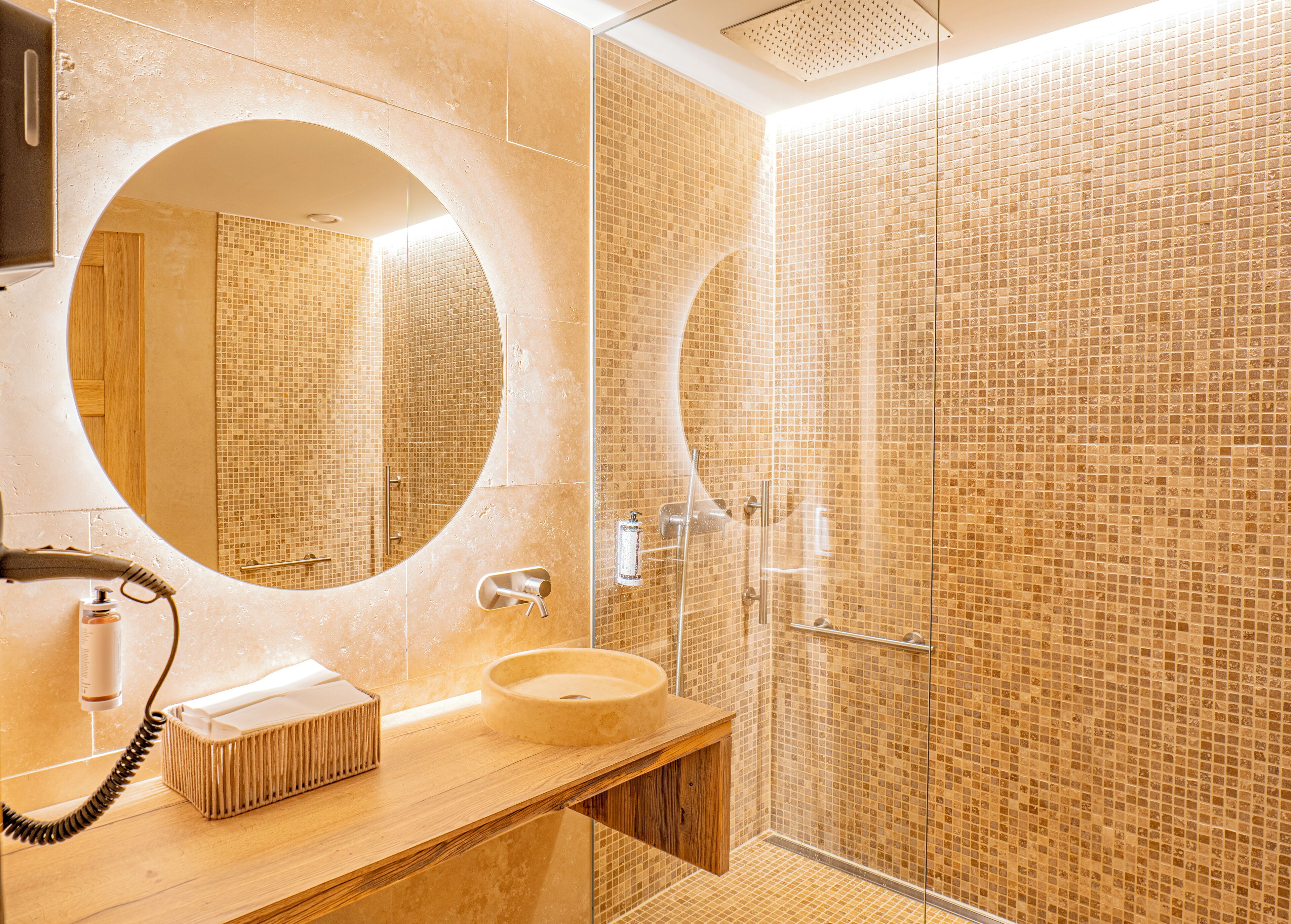 Un baño con espejo redondo, lavamanos y zona de ducha con paredes de azulejos.