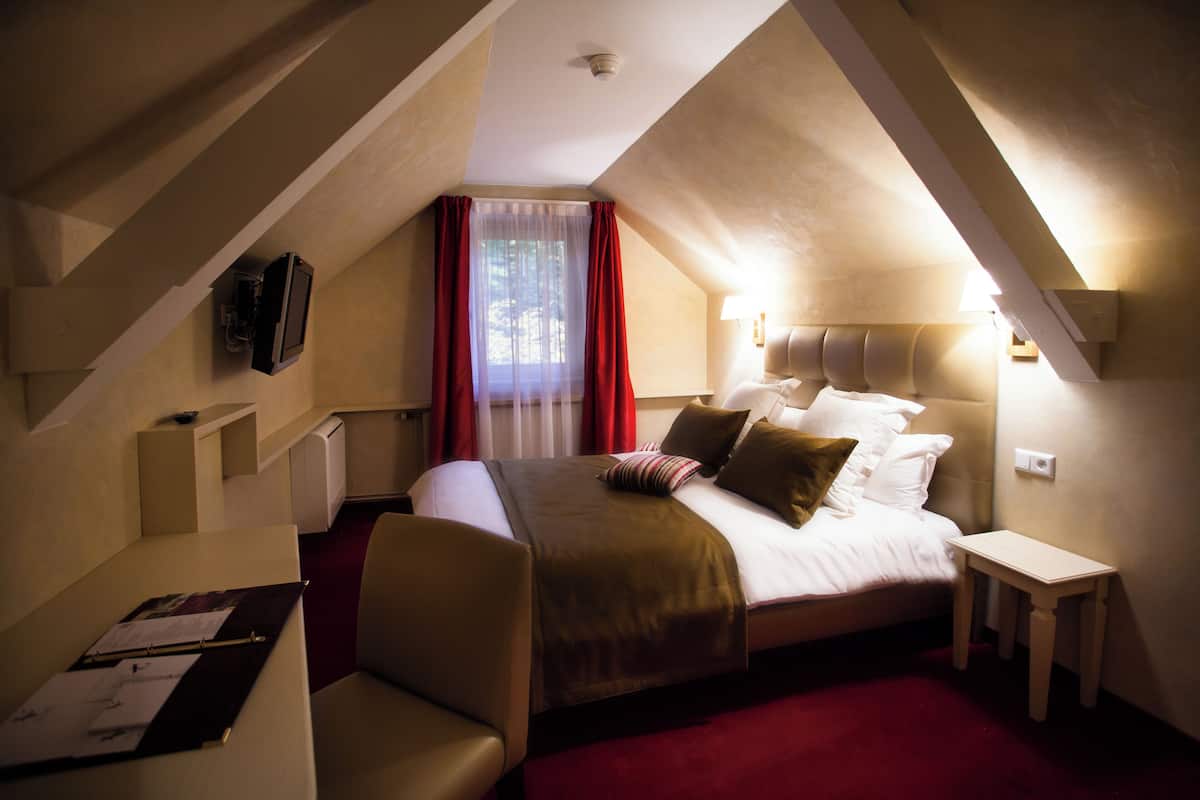 A hotel room with a bed, a desk, and a television mounted on the wall.
