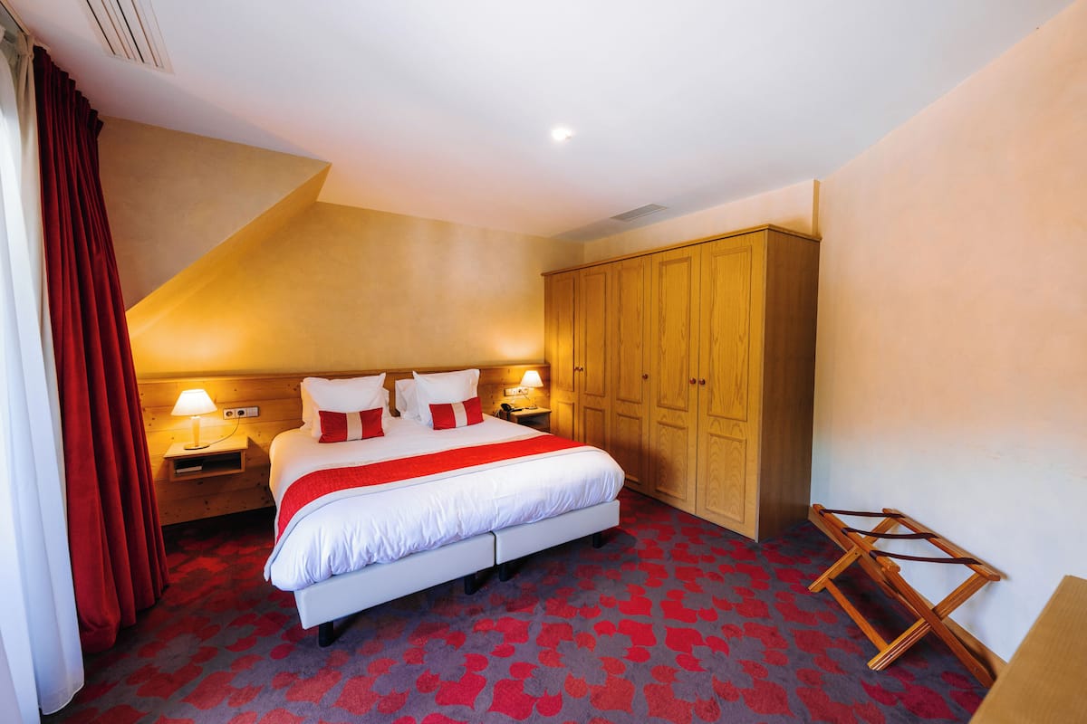 A hotel room with a large bed, wooden wardrobe, and a red carpet.
