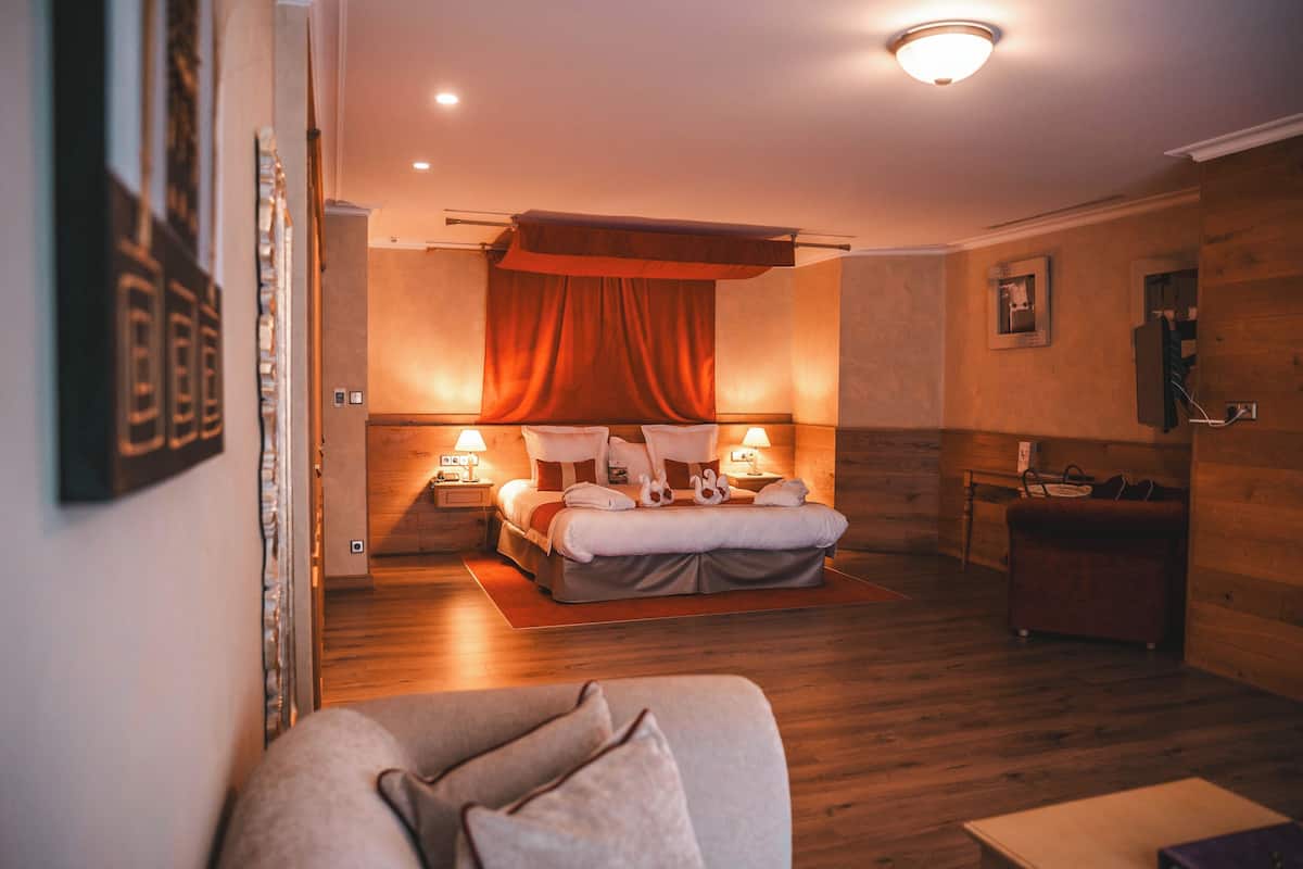A modern hotel room with a large bed, a wooden floor, a sitting area with a sofa, and a small table.