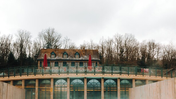 A couple in a hot tub with a wooden deck and a building in the background. - Hôtel & SPA Les Violettes (Soultz-Haut-Rhin)