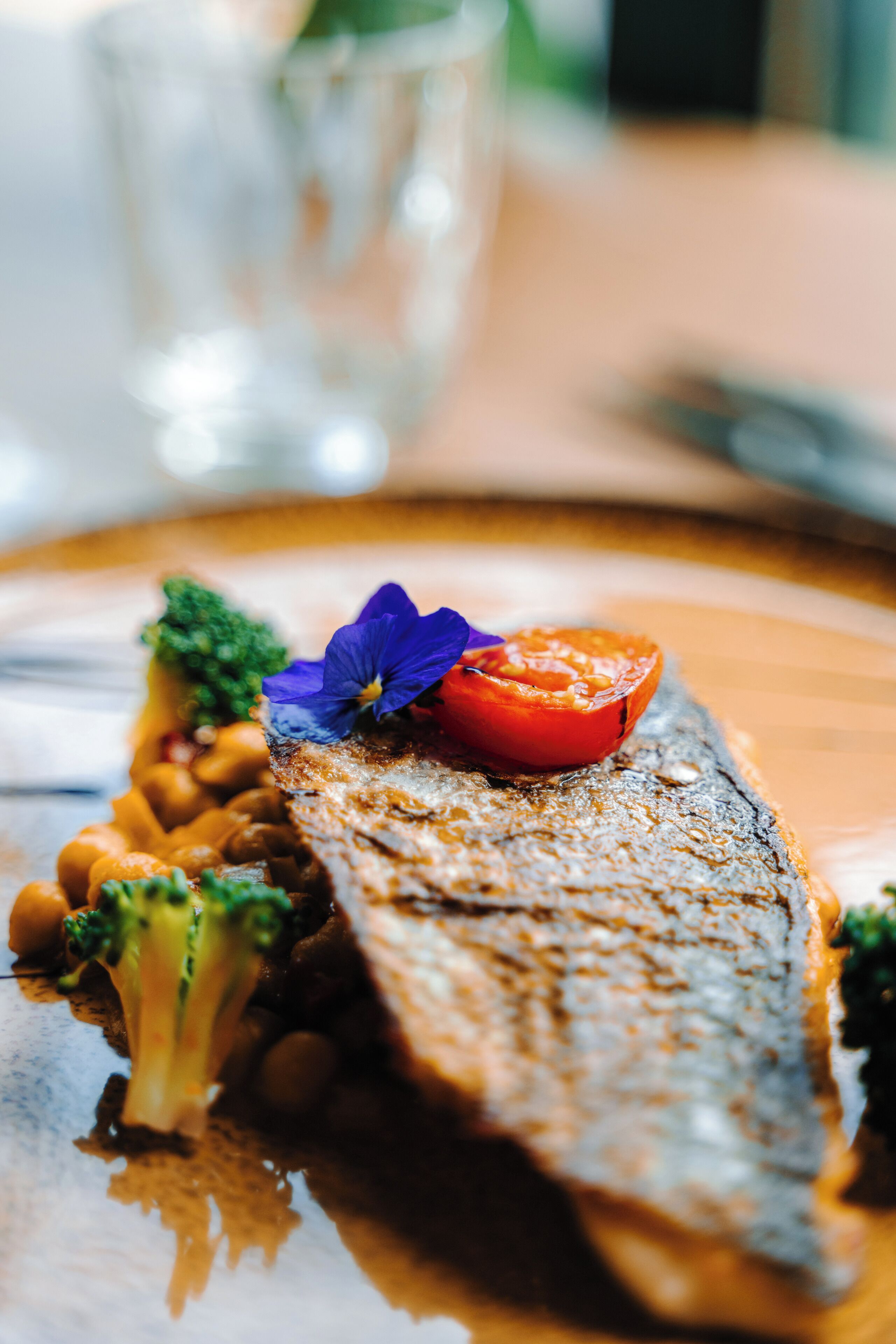 Un piatto con un pesce alla griglia, broccoli e una fetta di pomodoro.