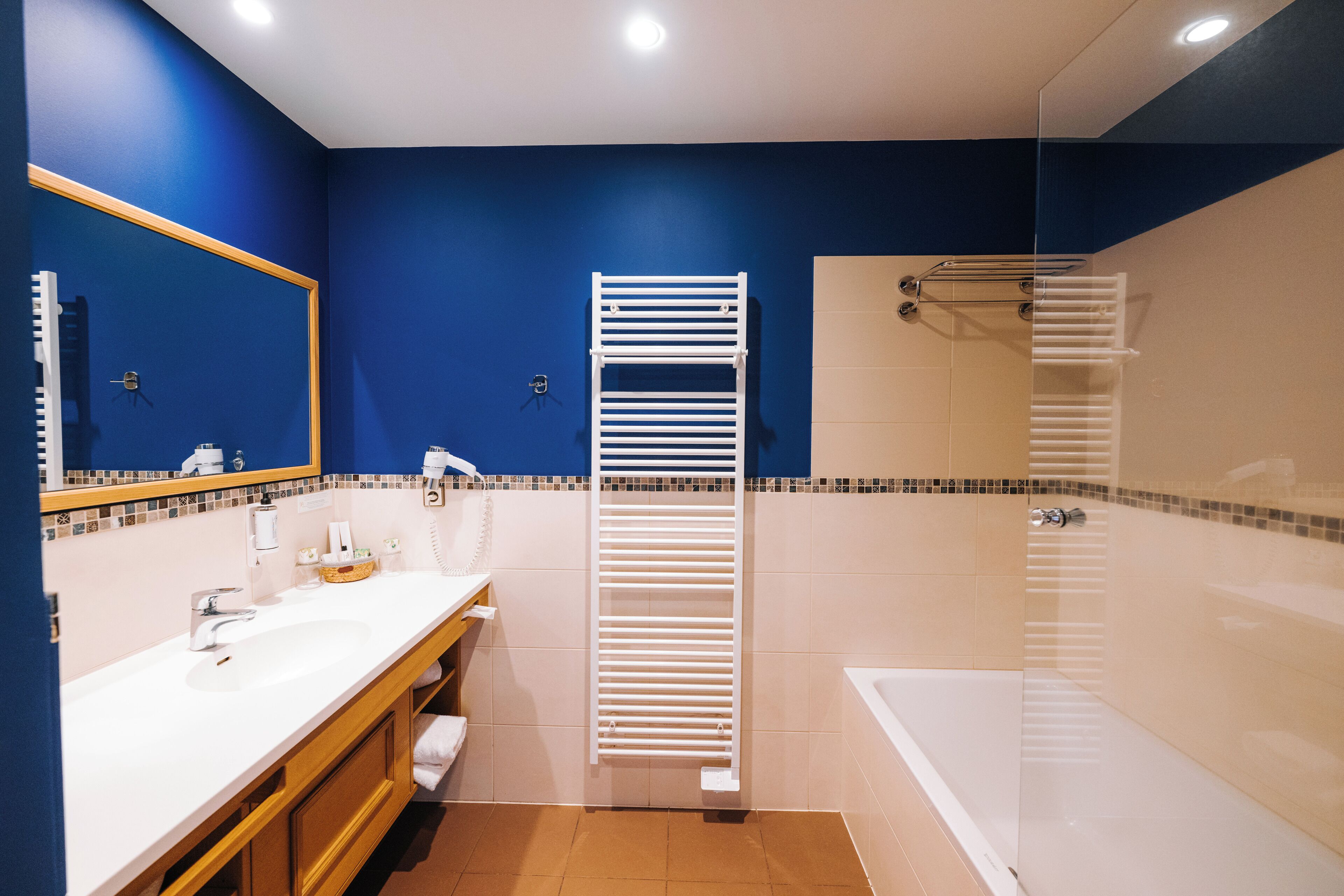 A modern bathroom with a blue wall, a white sink, a glass shower enclosure, and a white towel rack.
