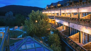 A multi-story hotel with a glass conservatory, outdoor seating, and a mountain backdrop. - Hôtel & SPA Les Violettes (Soultz-Haut-Rhin)
