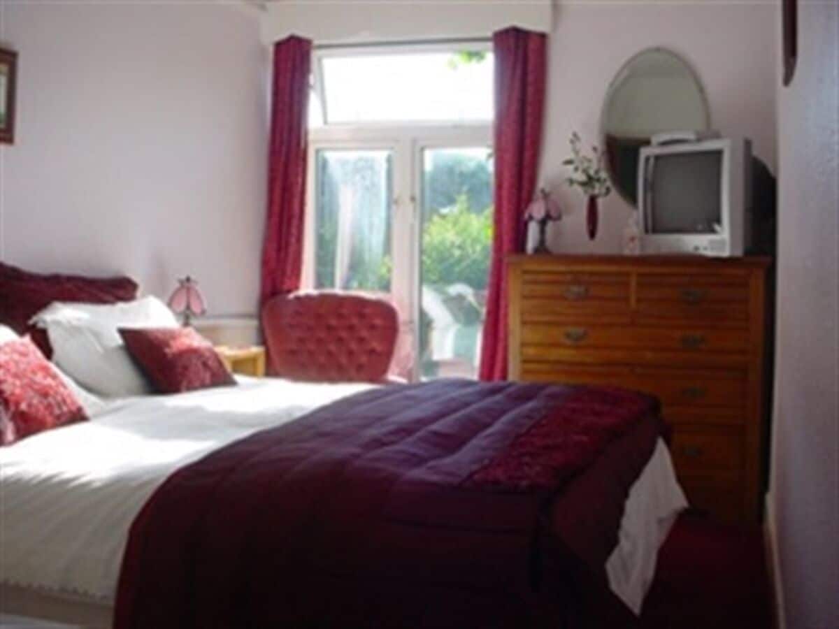 A bedroom with a bed, a dresser, a television on top of the dresser, and a window with curtains.