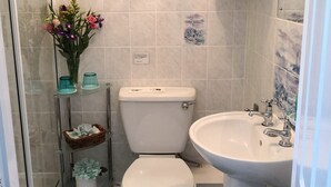 Ein Badezimmer mit Toilette, Waschbecken und Dusche. Auf einem Regal steht eine Vase mit Blumen.