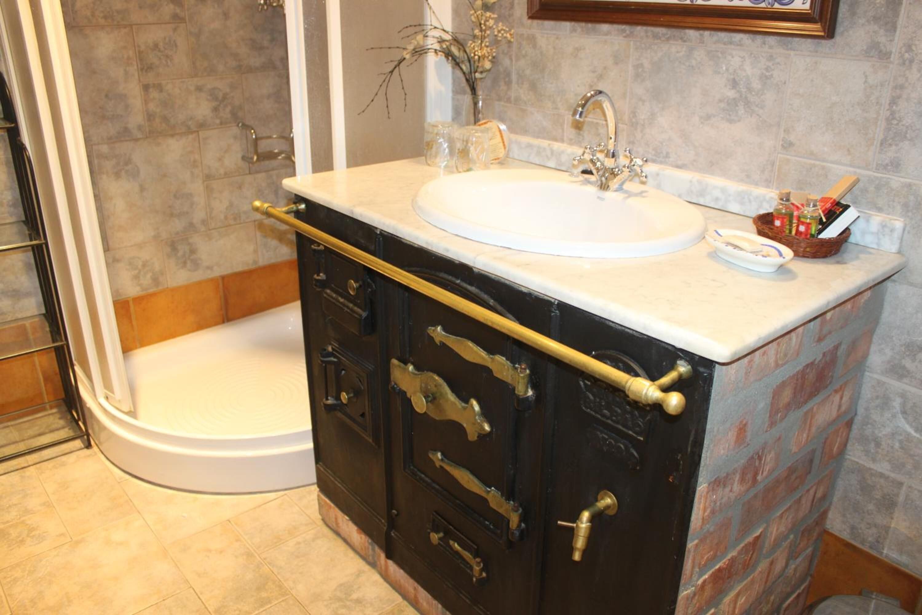Un baño con un lavamanos blanco, un mueble negro con tiradores de latón y una zona de ducha.