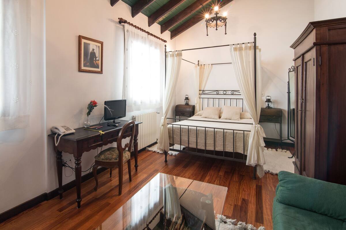A bedroom with a four-poster bed, a desk with a computer, a telephone, and a chair.