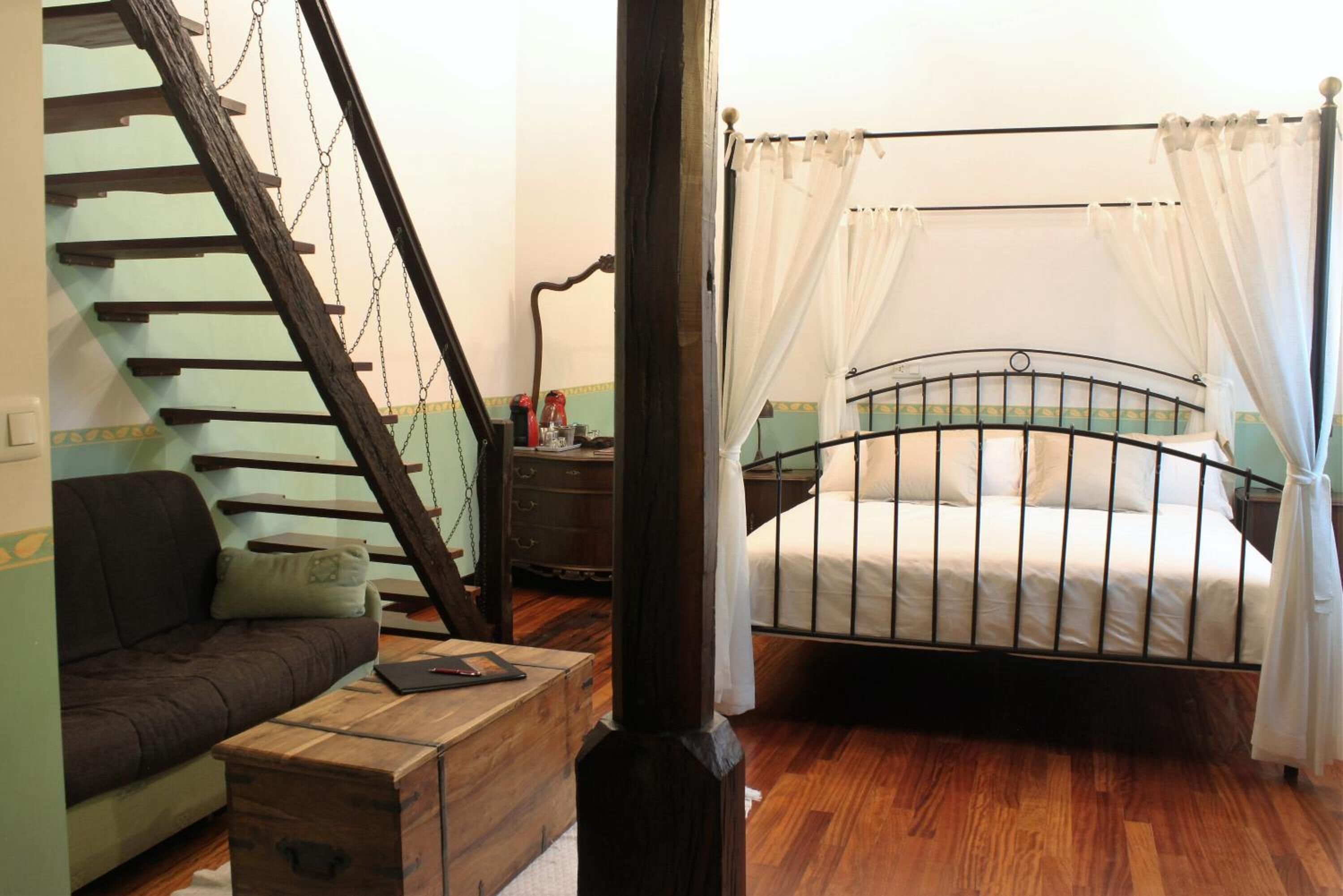 A bedroom with a wooden staircase, a bed with a metal frame, and a wooden chest of drawers.