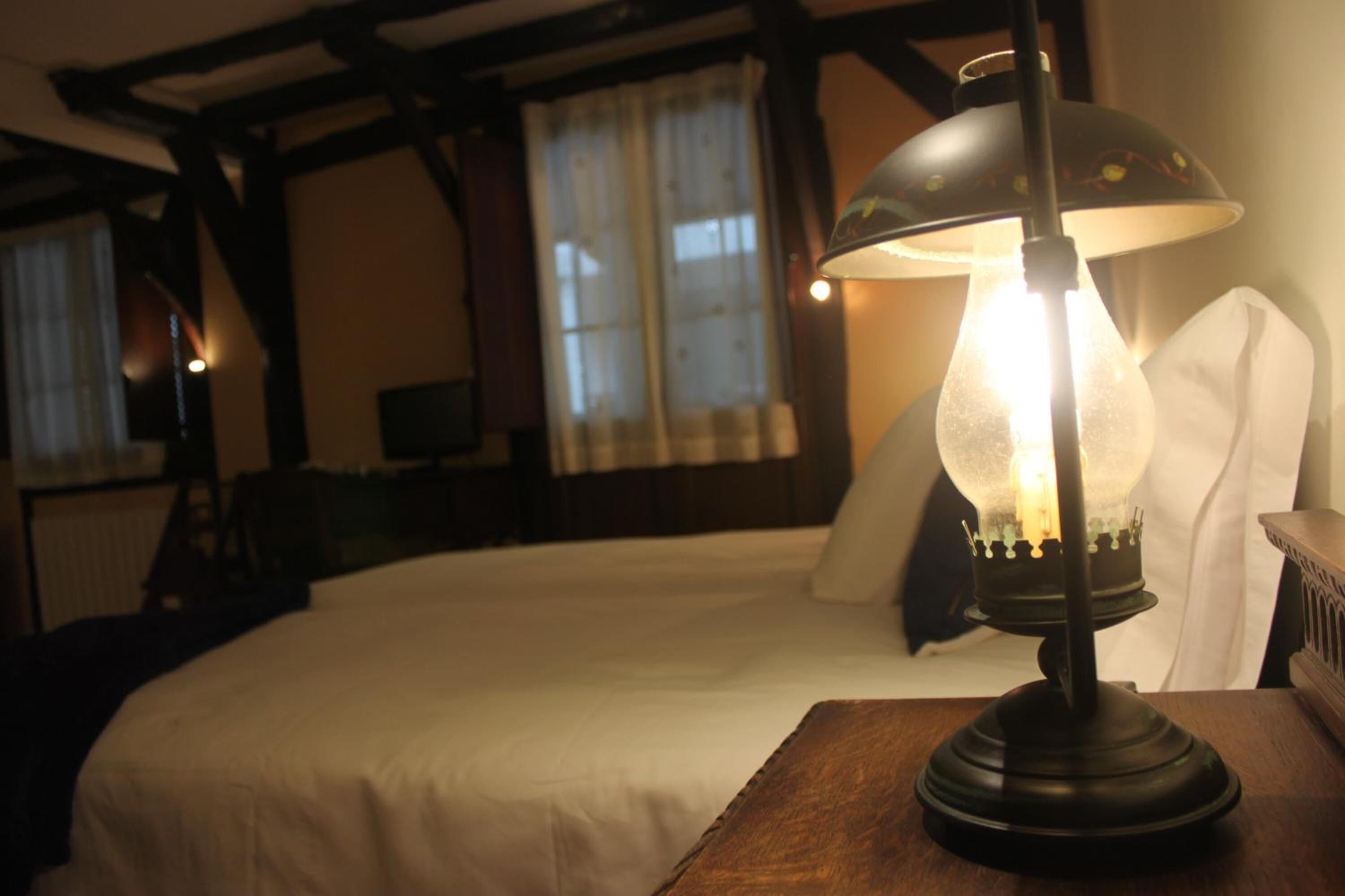 Une pièce avec un lit, une lampe posée sur une table en bois et une fenêtre avec des rideaux.