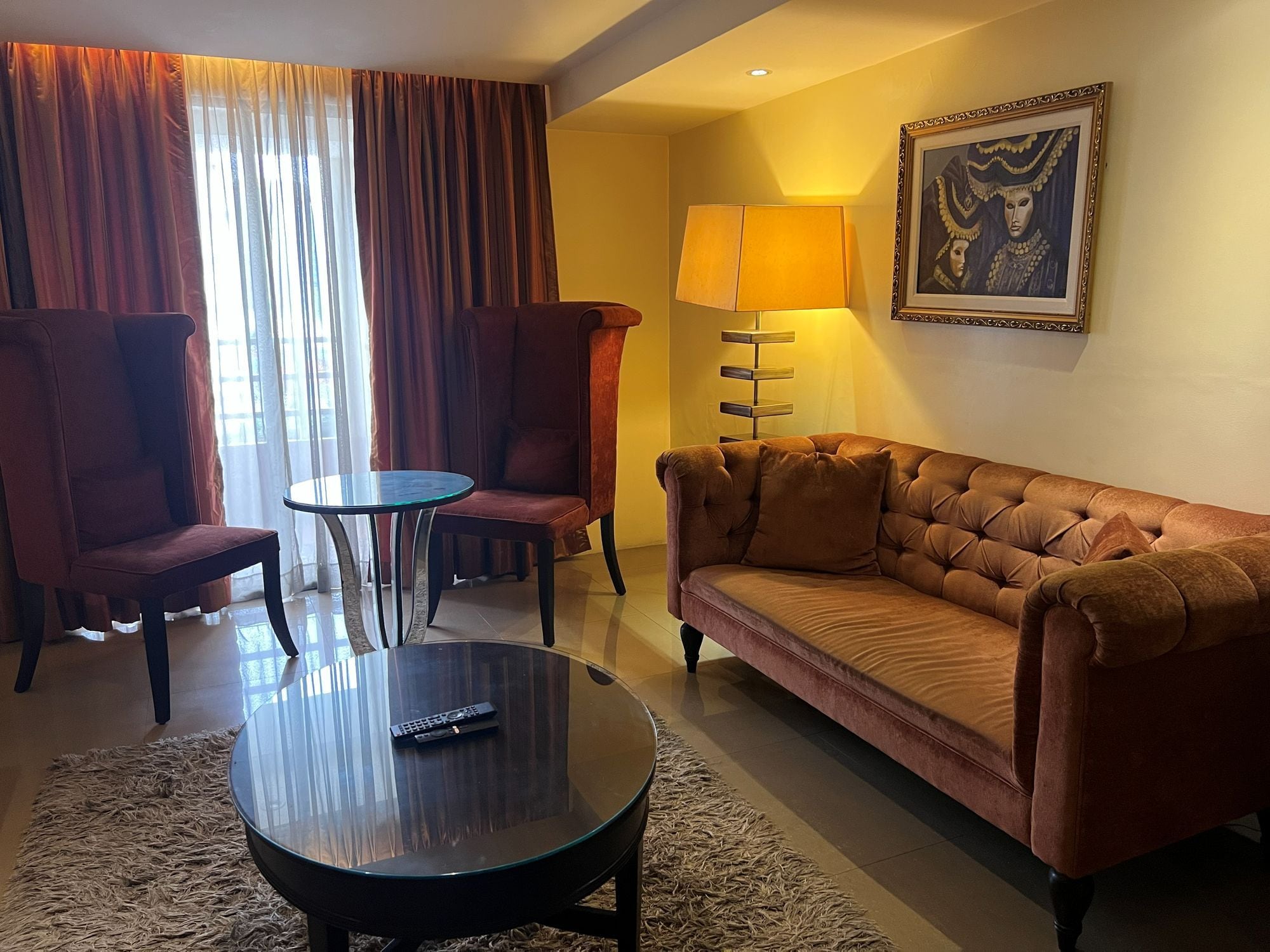 Une chambre d’hôtel avec un canapé, deux fauteuils, une table basse et une lampe.