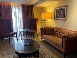 A hotel room with a sofa, two armchairs, a coffee table, and a lamp.