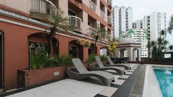 Un hotel con piscina, sillones de descanso y un jardín con palmeras.