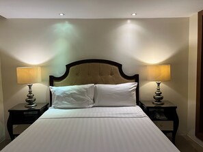 A hotel room with a large bed, two bedside lamps, and a headboard.