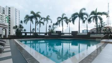 Una piscina con un borde de baldosas, rodeada de palmeras y un rascacielos al fondo.