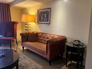 A living room with a brown sofa, a lamp, a framed artwork, a telephone, and a chair. - Palette Torre Venezia Suites (Quezon City)