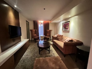 A modern living room with a flat-screen TV, a sofa, two armchairs, a coffee table, and a rug. - Palette Torre Venezia Suites (Quezon City)