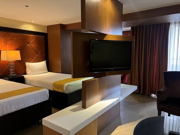 A hotel room with two beds, a flat-screen TV mounted on the wall, a bedside table, and a chair.