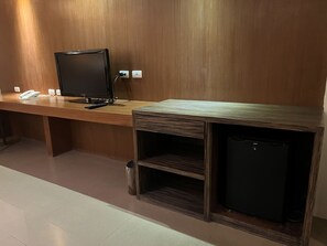 A wooden reception desk with a flat-screen TV, a telephone, and a small refrigerator.