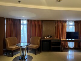 A hotel room with a seating area, a television, and a small kitchenette.