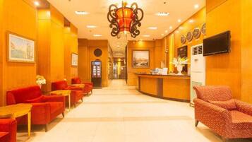 A hotel lobby with red seating, a reception desk, and a chandelier.