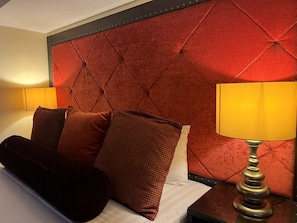 A hotel room with a tufted headboard, a bed with multiple pillows, a bedside table with a lamp, and a wall-mounted light. - Palette Torre Venezia Suites (Quezon City)