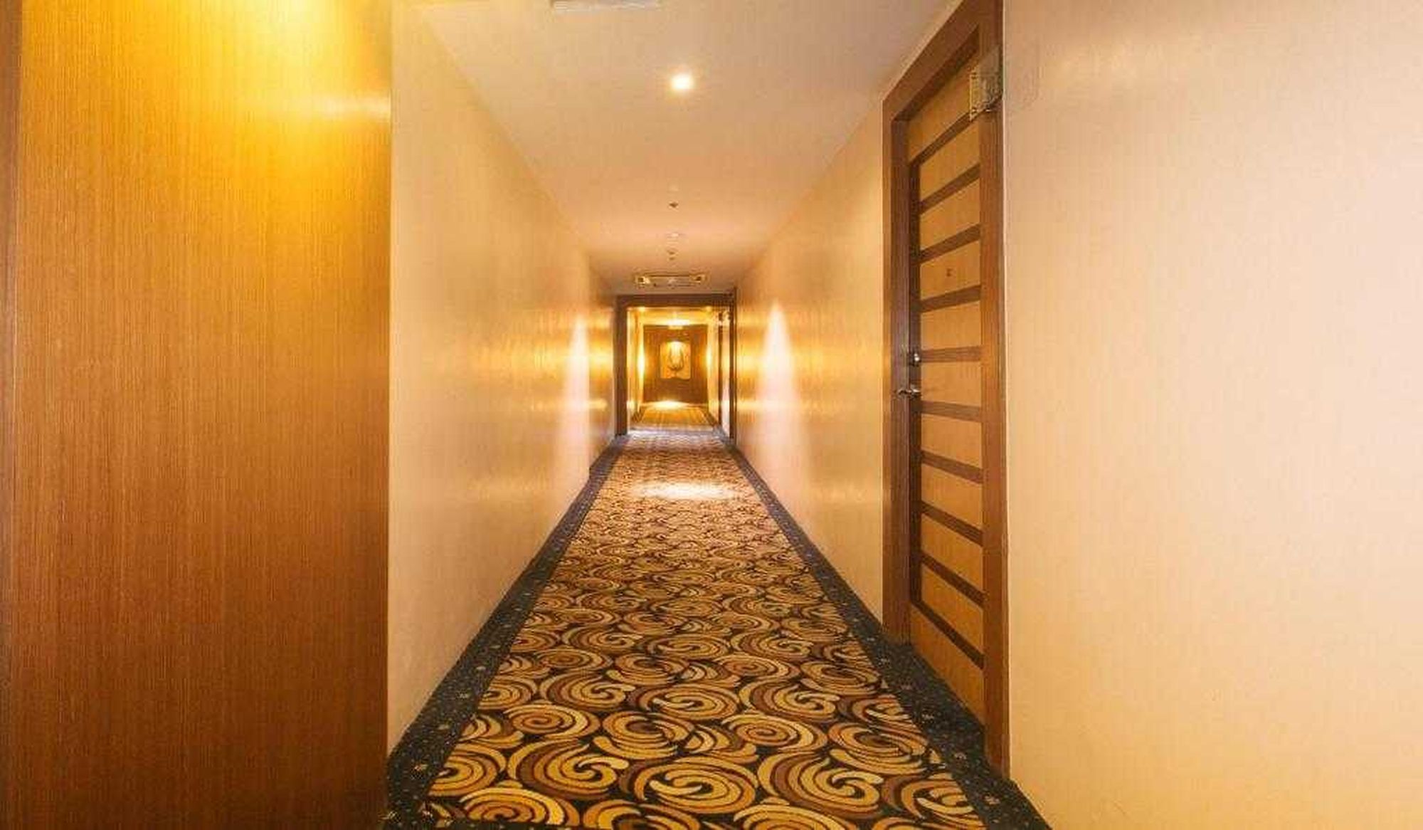 Un couloir d’hôtel avec un tapis à motifs et des portes en bois.