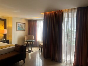 A hotel room with a bed, a chair, a small table, and a painting on the wall.