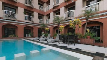 Un hotel con piscina, sillas de descanso y un patio con plantas.