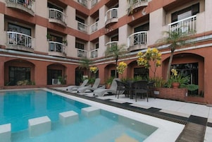 A hotel with a swimming pool, lounge chairs, and a patio area with plants.